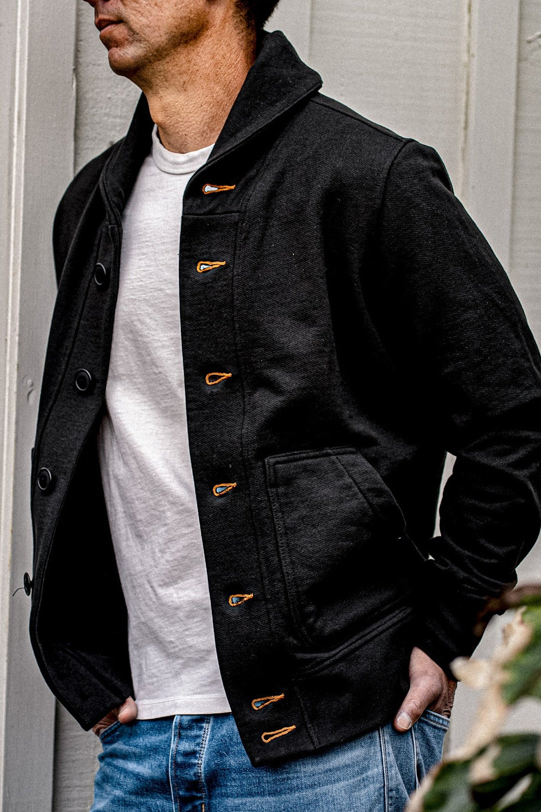 Man wearing a black shawl-collar French terry cardigan with tobacco-orange contrast keyhole stitching over a white tee and.
