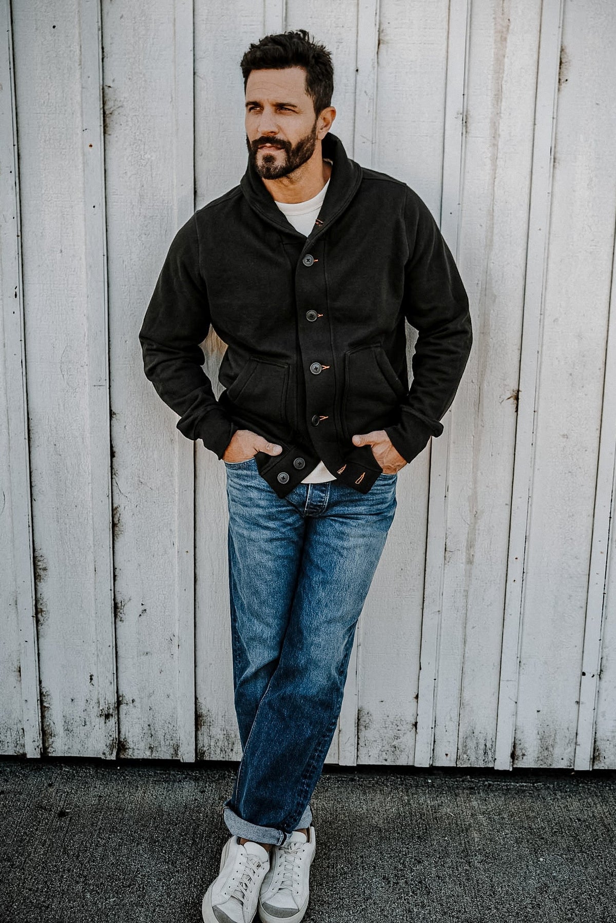 Man leaning against a wall wearing a men's basalt French terry cardigan with cuffed jeans and white sneakers