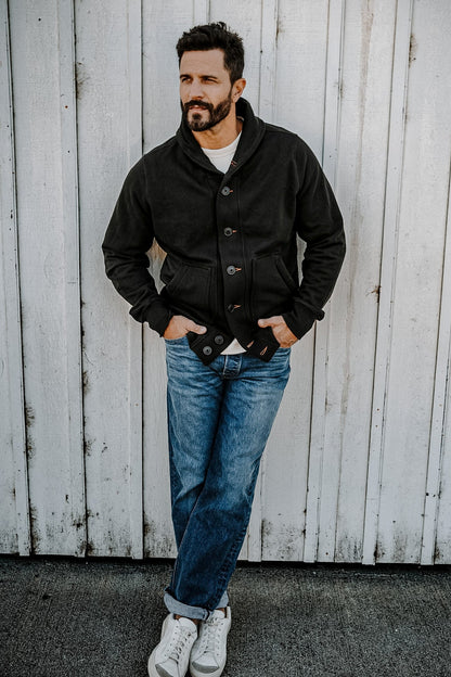 Man leaning against a wall wearing a men's basalt French terry cardigan with cuffed jeans and white sneakers