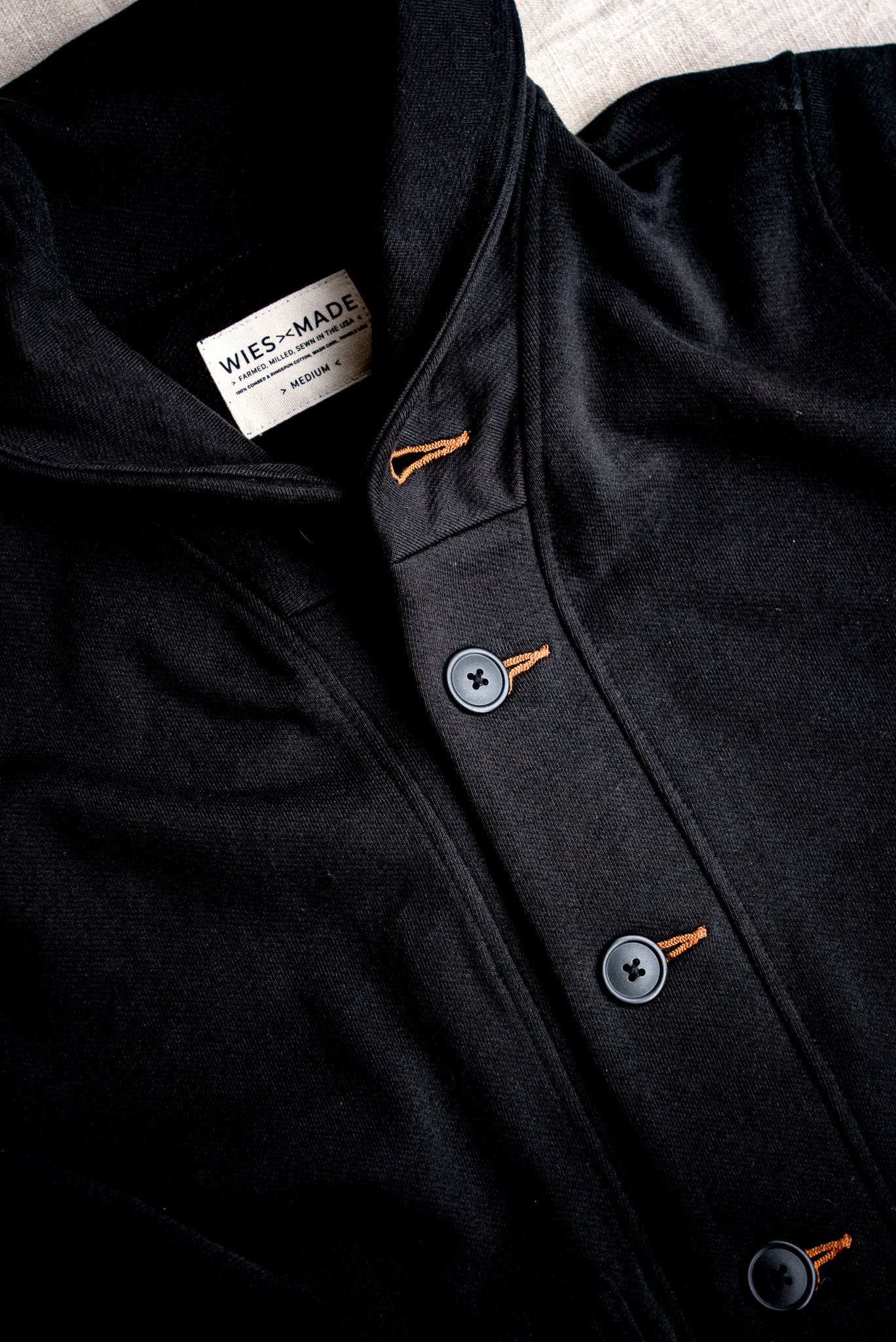 Close-up of the Bodega shawl cardigan in black French terry with tobacco-thread keyhole buttonholes and WiesMade label.
