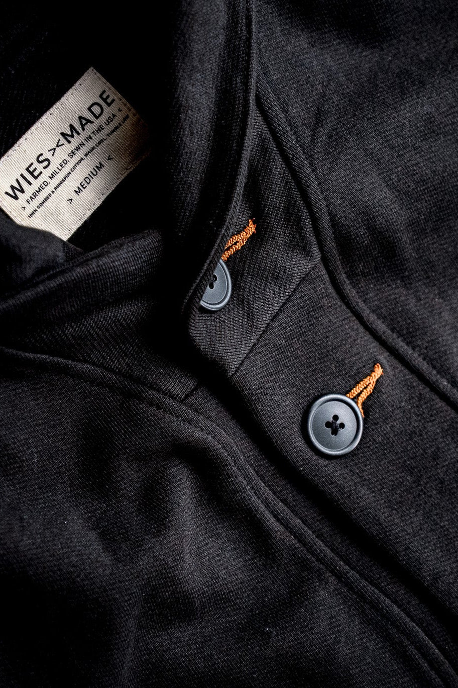 Close-up of basalt black French terry cardigan showing gray buttons, tobacco contrast keyhole stitching, and WiesMade inner.