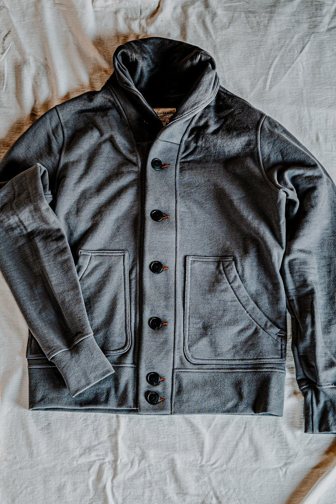 Men's pebble French terry cardigan laid flat, showing the shawl collar, button-front closure, and patch pockets