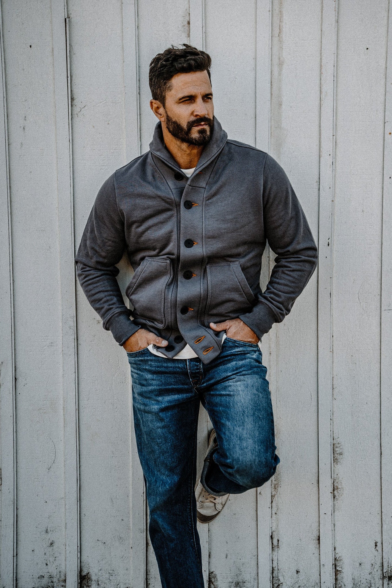 Man standing against a wood plank wall wearing a men's pebble French terry cardigan, looking to the side