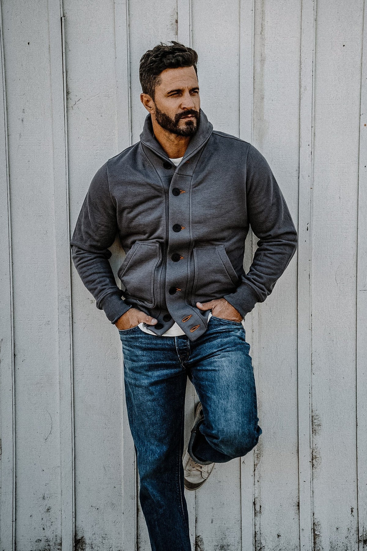 Man leaning against a wall wearing a men's pebble French terry cardigan with jeans