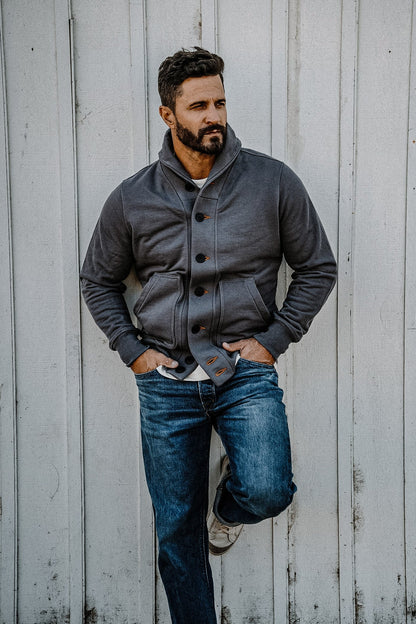Man leaning against a wall wearing a men's pebble French terry cardigan with jeans