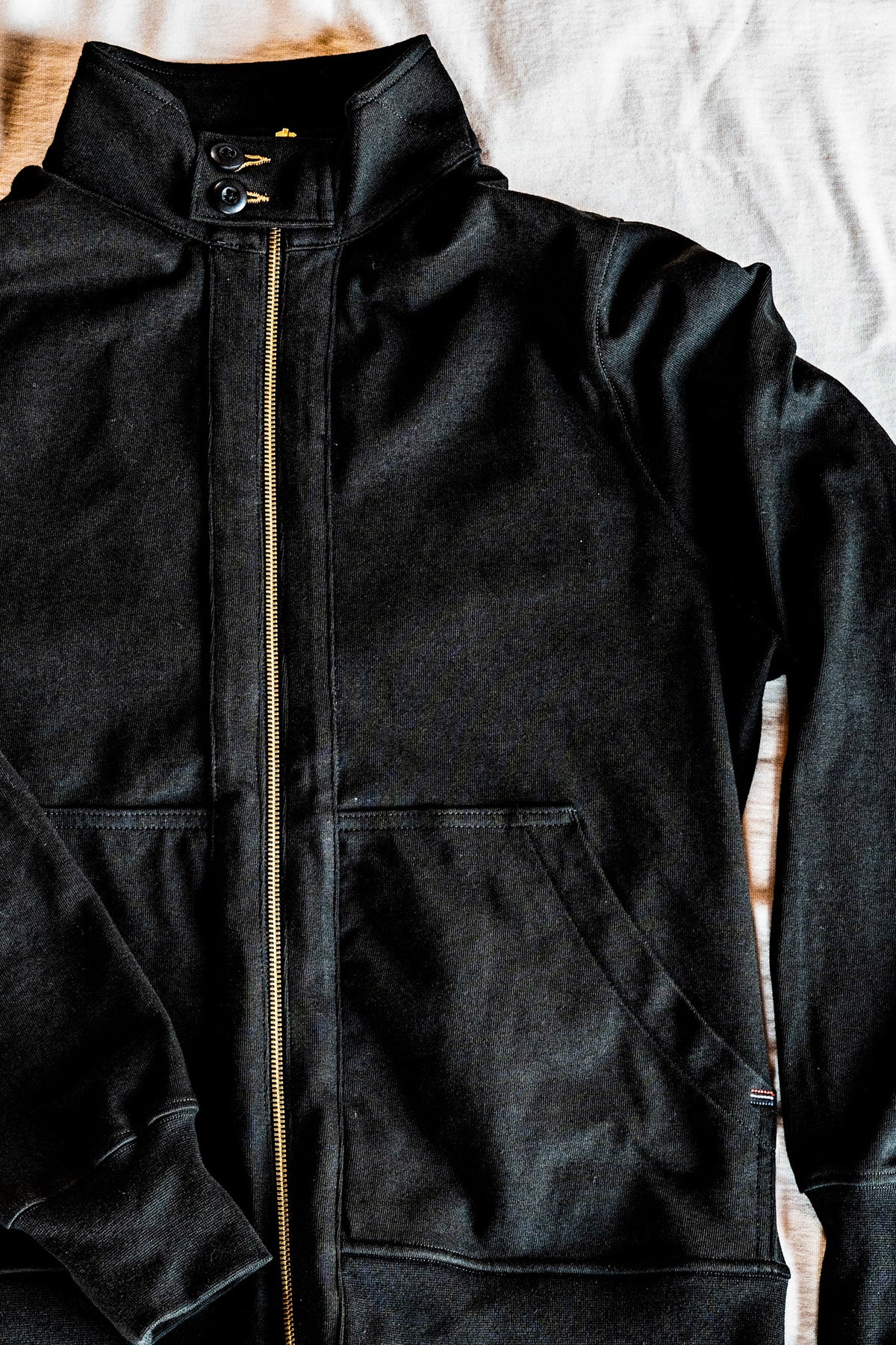 Close-up flat lay of a men's charcoal zip-up moto jacket showing the snap collar, zip front, and patch pocket detail