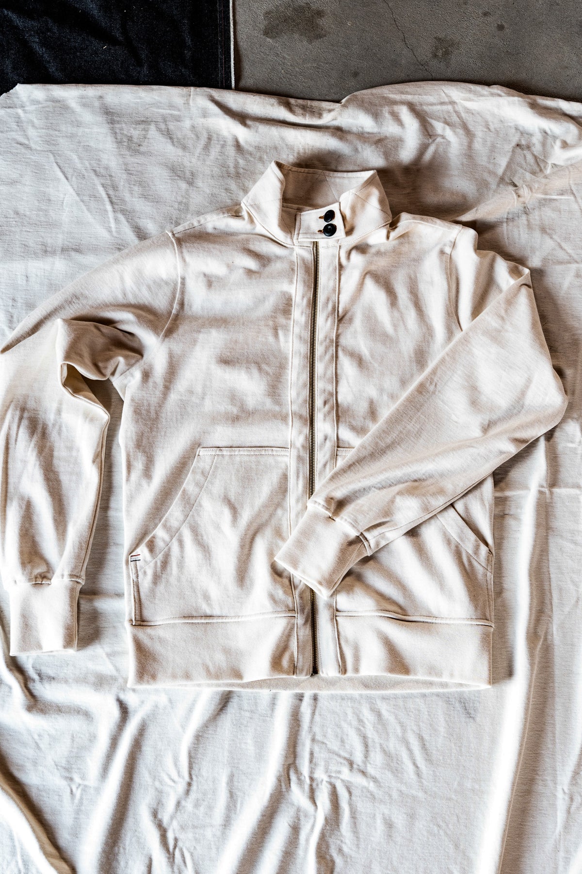 Natural cotton men's zip-up moto jacket laid flat on linen, showing the snap collar and front pocket