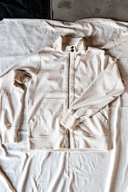 Natural cotton men's zip-up moto jacket laid flat on linen, showing the snap collar and front pocket