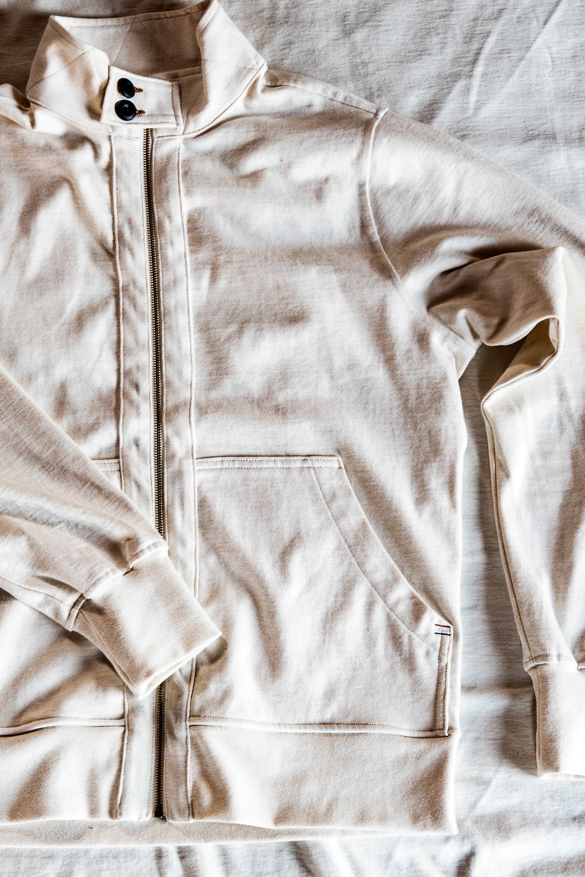 Flat lay of a men's cream zip-up moto jacket showing the snap collar and front pocket