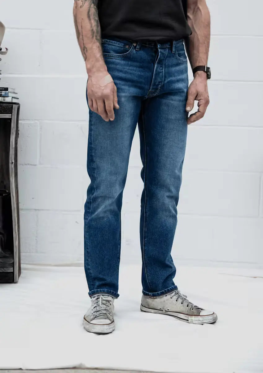 Sam Fit jeans in River Wash color, worn by a man, featuring a standard fit with a clean, faded finish & straight-leg style