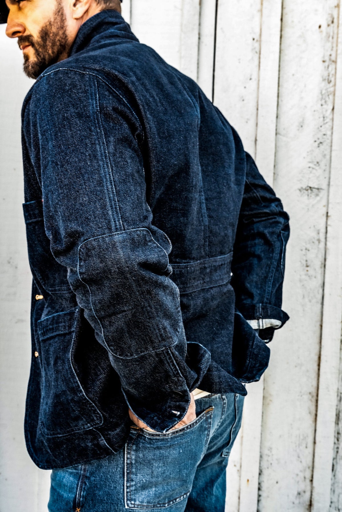 Back view of a man wearing a men's ocean denim chore blazer, showing the back seam and patch pocket detail