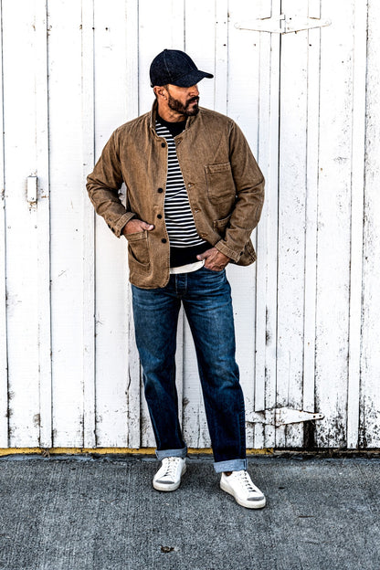 Man standing in a men's wheat denim chore blazer and jeans, hand in pocket, looking to the side