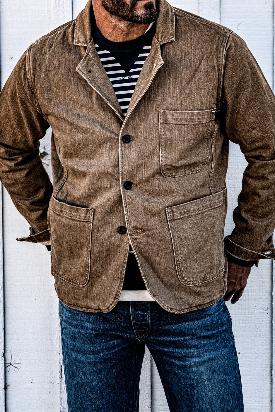 Close-up of a man in a cap wearing a buttoned men's wheat denim chore blazer with hands clasped
