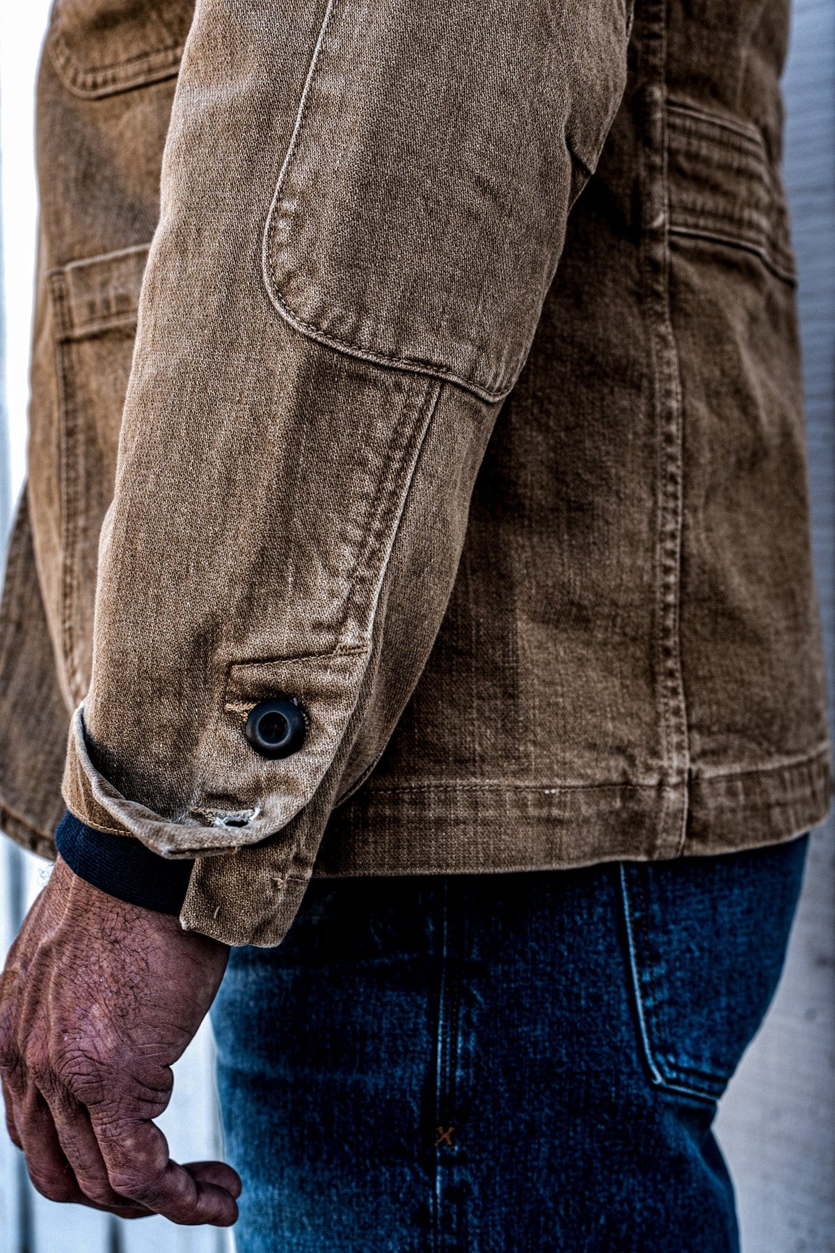 Close-up of the side vent and hem button detail on a men's wheat denim chore blazer