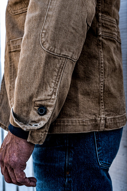 Close-up of the side vent and hem button detail on a men's wheat denim chore blazer