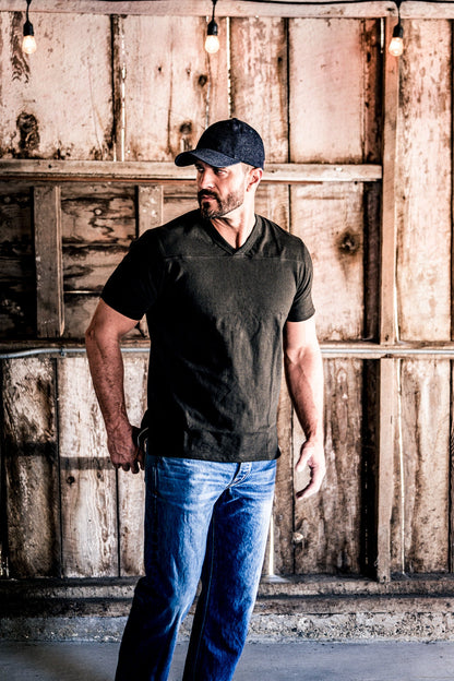 Man wearing a men's basalt V-neck cotton jersey top and jeans standing under string lights in a barn