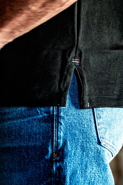 Close-up of the side hem and vent detail on a men's basalt cotton jersey top worn over blue denim jeans