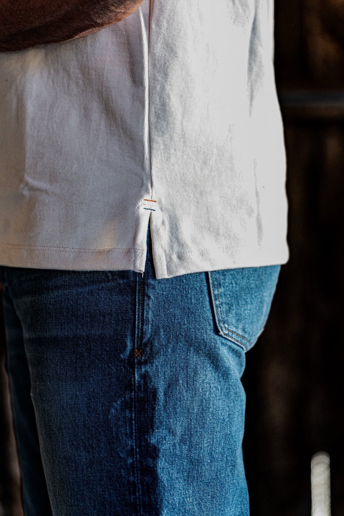 Close-up of the side hem and vent detail on a men's natural cotton jersey top worn over blue denim jeans