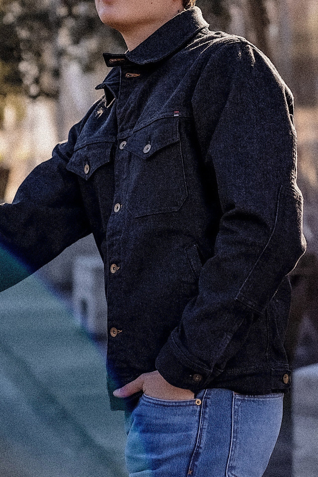 14oz broken twill denim jacket in black with button closures and chest pockets, worn over blue jeans in an outdoor setting.