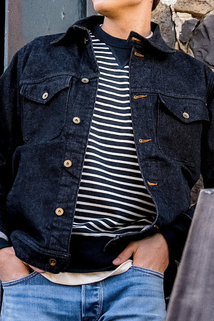 Made in USA denim jacket in black with button closures and chest pockets, layered over a striped sweater and blue jeans.