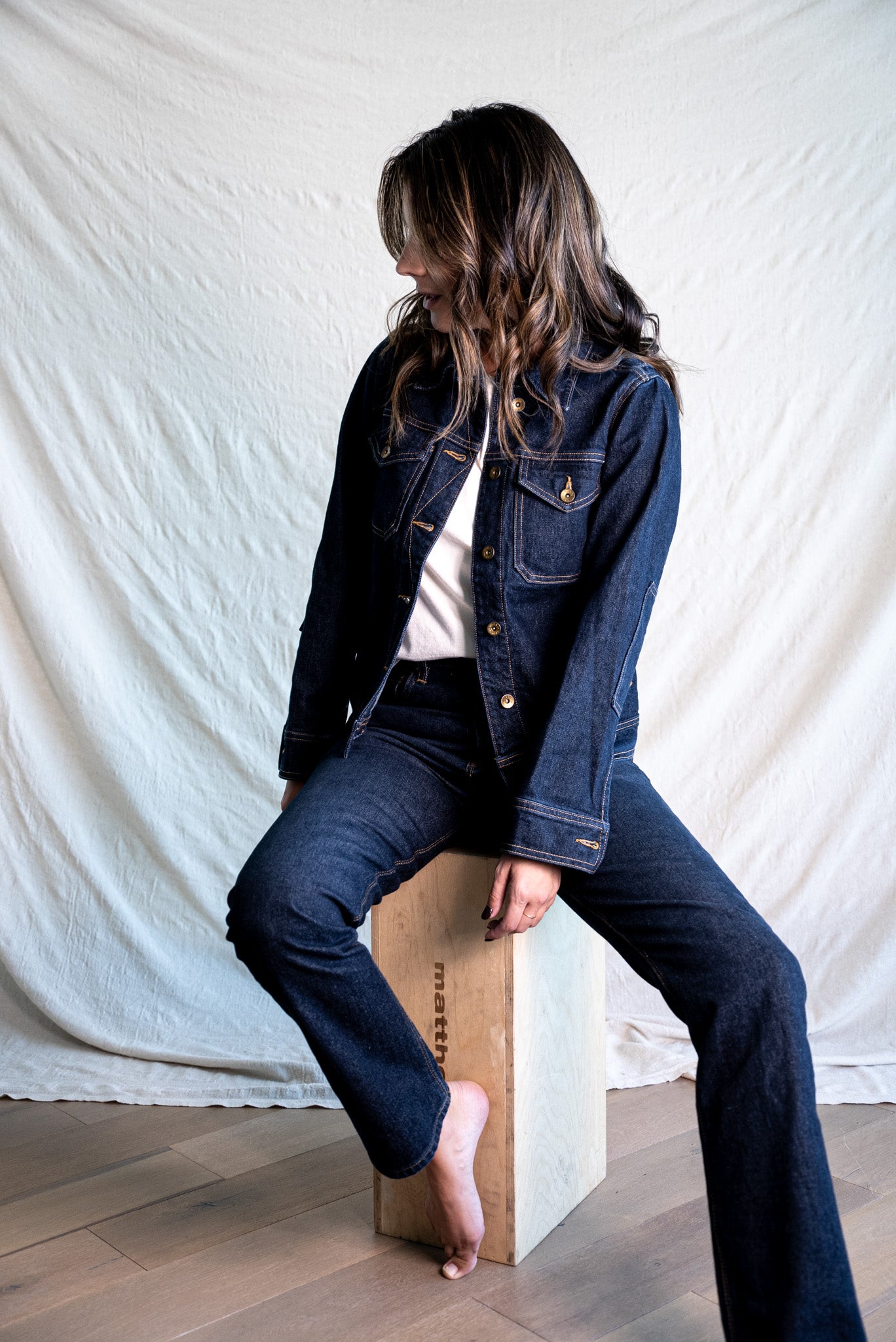 Dark denim jacket made in USA paired with matching jeans, styled casually while seated on a wooden box.