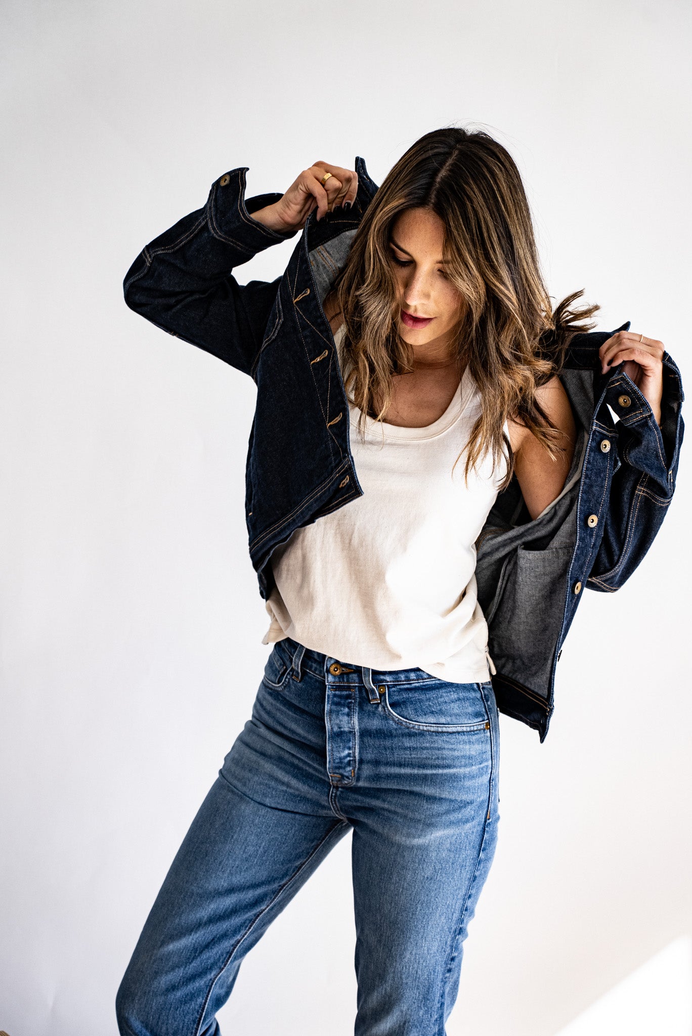 American made denim jacket layered over a white tank top and paired with high-waisted jeans, styled casually.