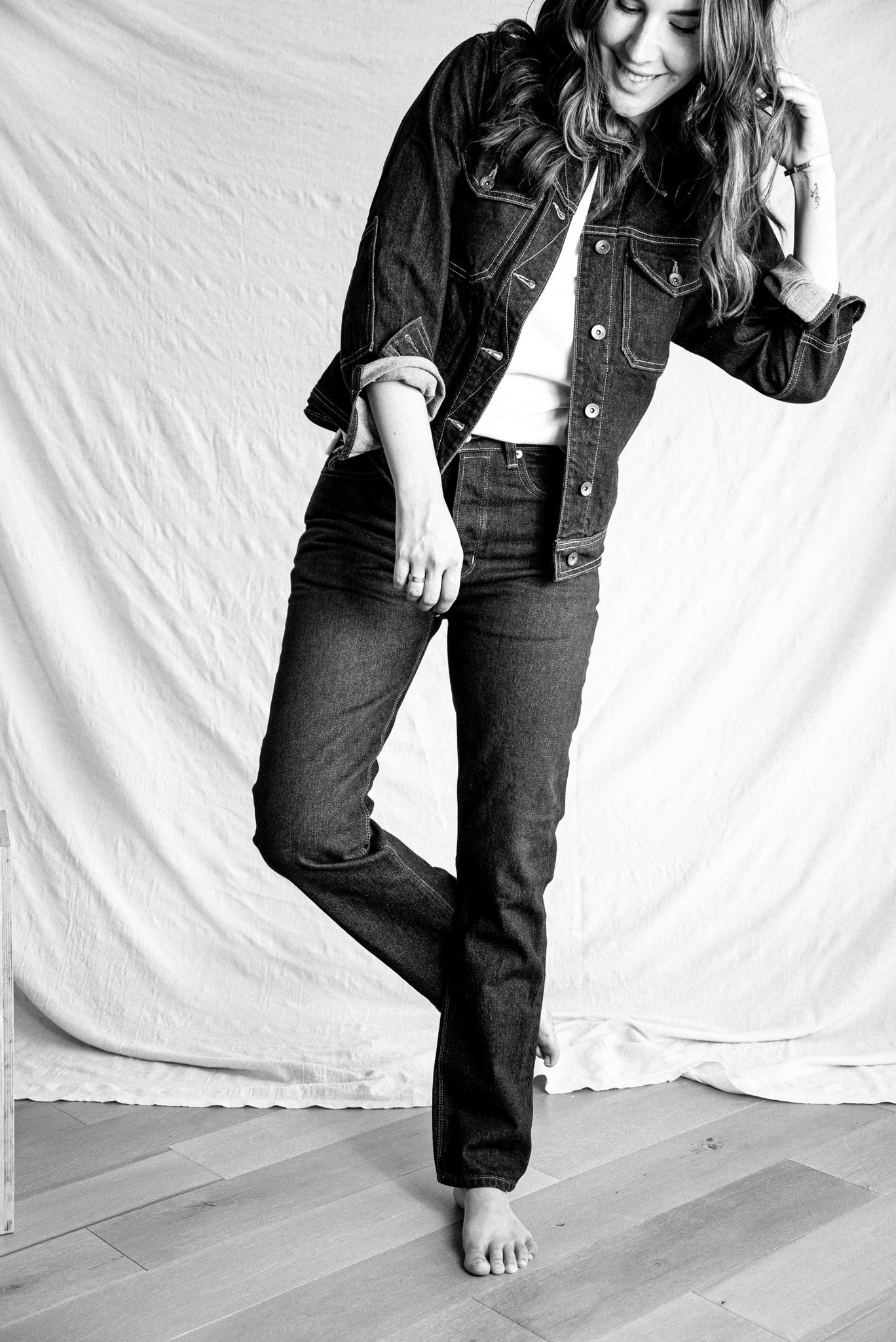 American made jean jacket paired with dark denim jeans, styled barefoot in a minimalist black and white portrait.