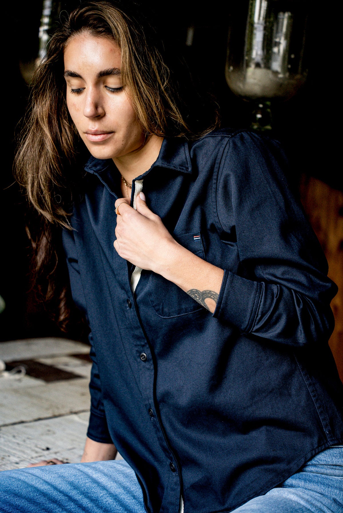 Close view of a women's navy cotton overshirt with a hand adjusting the collar and placket.