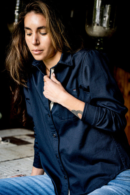 Close view of a women's navy cotton overshirt with a hand adjusting the collar and placket.
