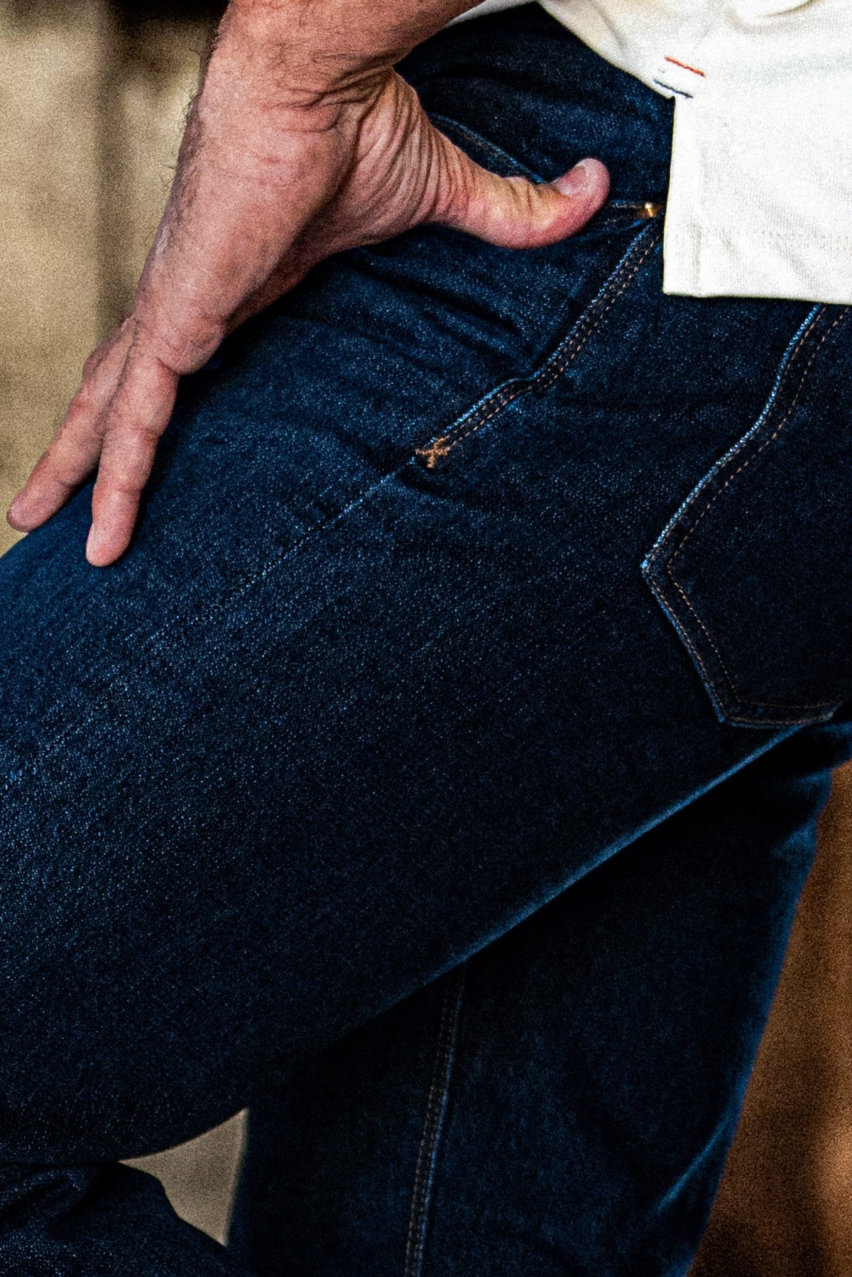 Close-up of men's dark wash slim straight jeans with a hand resting on the back pocket.