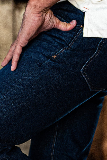 Close-up of men's dark wash slim straight jeans with a hand resting on the back pocket.