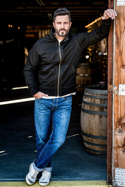 Man wearing a men's charcoal zip-up moto jacket and cuffed jeans posing in a wine cellar doorway