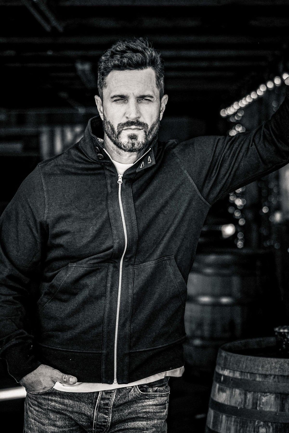 Black and white close-up portrait of a man wearing a men's zip-up moto jacket in a wine cellar