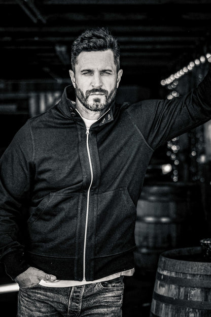 Black and white close-up portrait of a man wearing a men's zip-up moto jacket in a wine cellar