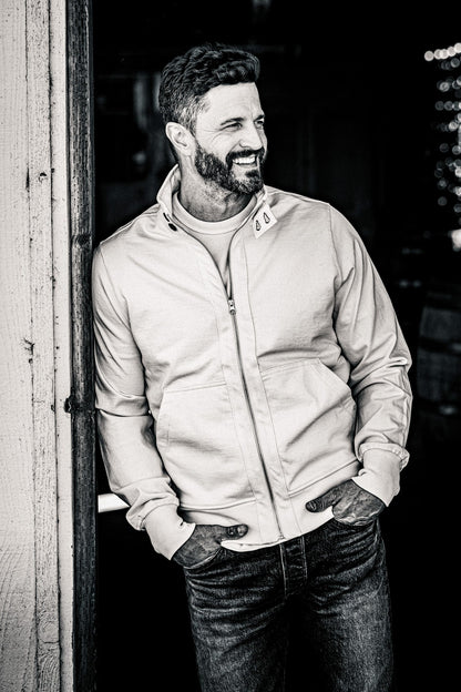 Black and white photo of a man in a men's zip-up moto jacket and jeans in a barn doorway
